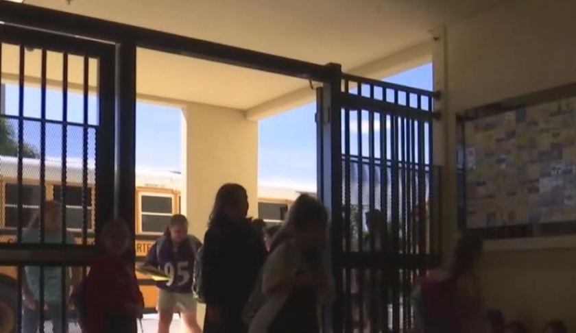 Children walking through an entrance way that is now locked during the school session, with surveillance technology monitoring nearby. Photo via WINK News.
