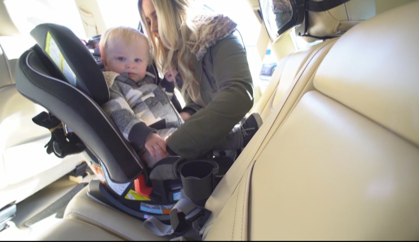 Mother properly secures child in car seat. Photo via CBS.
