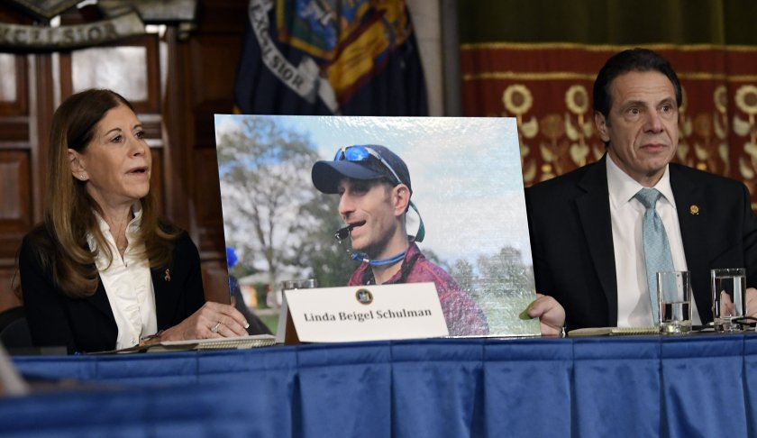 FILE - In this Tuesday, Jan. 29, 2019, file photo, Linda Beigel Schulman, left, holds a photograph of her son Scott Beigel, who was killed during the Valentine’s Day massacre at Marjory Stoneman Douglas High School, while speaking with New York Gov. Andrew Cuomo and gun safety advocates during a news conference at the state Capitol in Albany, N.Y. Since the shooting, states have seen a surge of interest in laws intended to make it easier to disarm people who show signs of being violent or suicidal. (AP Photo/Hans Pennink, File)