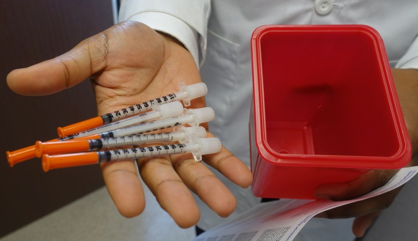 Doctor holds needles for exchange program. (CBS News photo)