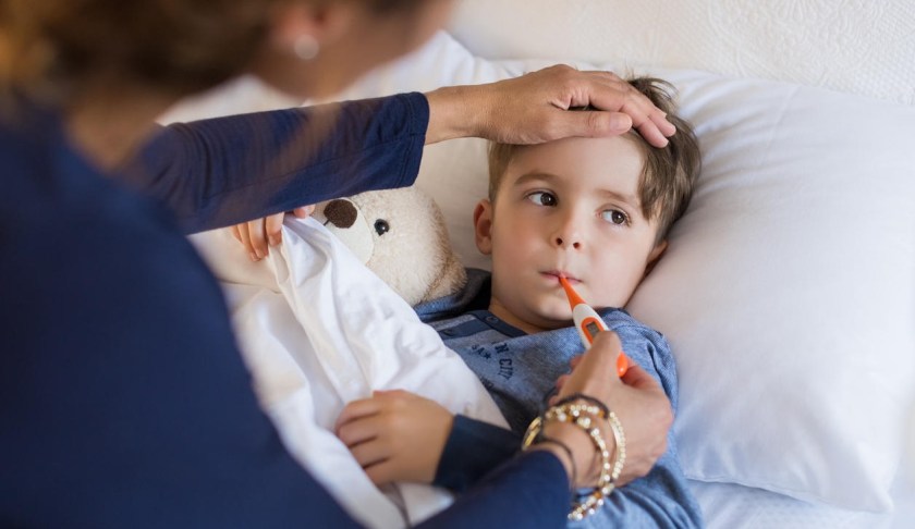 Sick boy laying in bed as his mother takes his temperature. (Credit: CBS News)