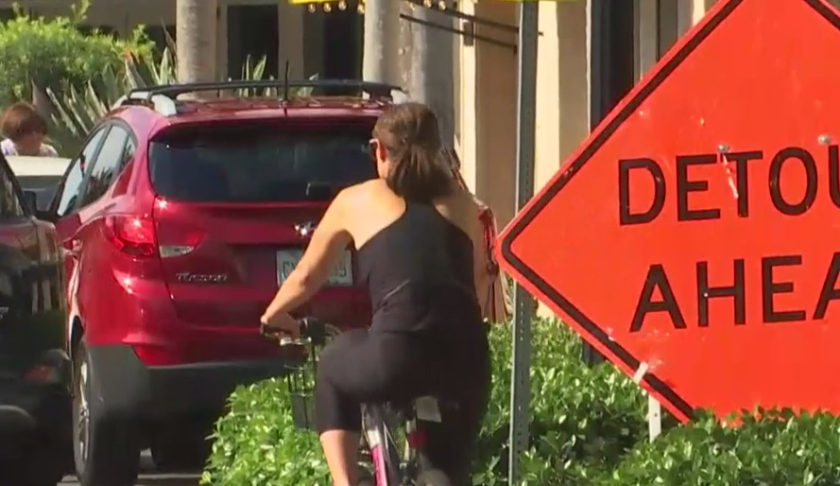 Cyclist peddles down the roadway adjacent to a detour ahead sign. (Credit: WINK News)