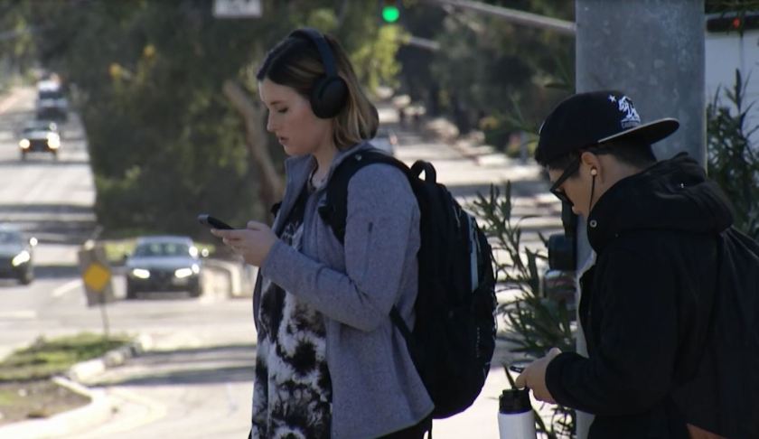 Teens on their phones while waiting to be picked up. (Credit: Ivanhoe Newswire)