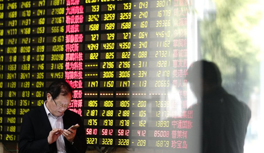 A man looks at his smartphone near a display showing stock prices at a brokerage house in Shanghai Monday, May 6, 2019. China's benchmark Shanghai Composite index dives on U.S. President Donald Trump threat of more China tariffs. At right is a reflection off a display board. (AP Photo)
