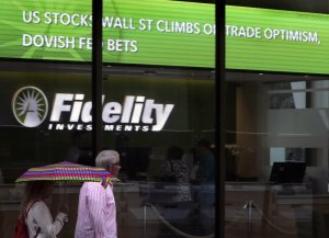 In this June 18, 2019, photo people walk past Fidelity Investments news scroll board, showing a favorable outlook in the US stock markets, in the Financial District of Boston. The Federal Reserve has decided that a rate cut now, and possibly one or more additional cuts to follow, could help inoculate the economy against a potential downturn. (AP Photo/Charles Krupa)