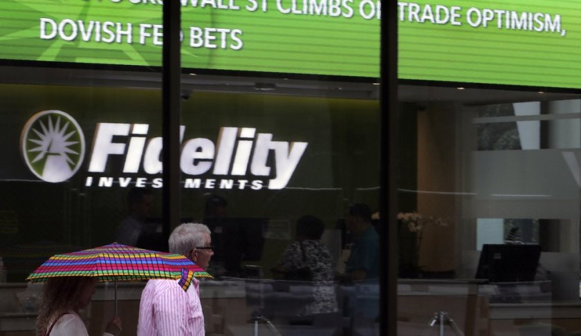 In this June 18, 2019, photo people walk past Fidelity Investments news scroll board, showing a favorable outlook in the US stock markets, in the Financial District of Boston. The Federal Reserve has decided that a rate cut now, and possibly one or more additional cuts to follow, could help inoculate the economy against a potential downturn. (AP Photo/Charles Krupa)