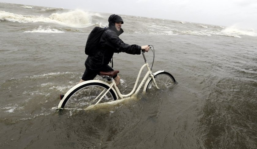 Tyler Holland guides his bike through the water as winds from Tropical Storm Barry push water from Lake Pontchartrain over the seawall Saturday, July 13, 2019, in Mandeville, La. (AP Photo/David J. Phillip)