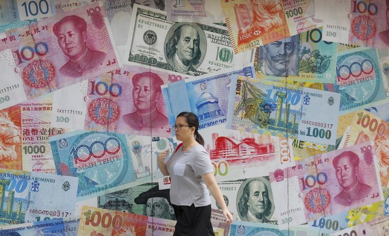 FILE - In this Aug. 6, 2019, file photo, a woman walks by a money exchange shop decorated with different countries currency banknotes at Central, a business district in Hong Kong. The Hong Kong stock exchange is dropping a bid to buy its London counterpart following opposition from the European exchange's management. Hong Kong Exchanges and Clearing Ltd. said it was "unable to engage" with the London exchange's management on the deal. (AP Photo/Kin Cheung, File)