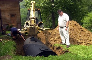 FILE: Tony Lewis, left, PRIDE coordinator in Perry County, watches as Paul Lewis maneuvers a septic tank into place Monday, July 15, 2002, in Happy, Ky. (AP Photo/Rhonda Simpson/FILE)