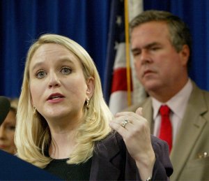 FILE - In this Tuesday, Sept. 28, 2004, file photo, Tiffany Carr, executive director of Florida Coalition Against Domestic Violence, left, speaks at a news conference held by Gov. Jeb Bush, background right, to announce a public awareness campaign designed to prevent disaster-related domestic violence, in Tallahassee, Fla. (AP Photo/Phil Coale, File)