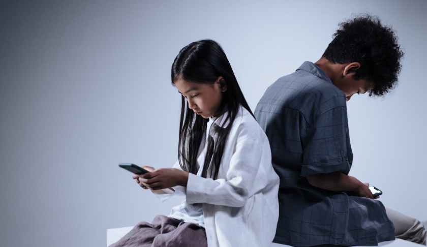 boy and girl sitting back to back holding smartphone