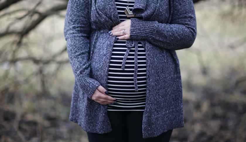 woman pregnant in black and white striped shirt standing near bare tree