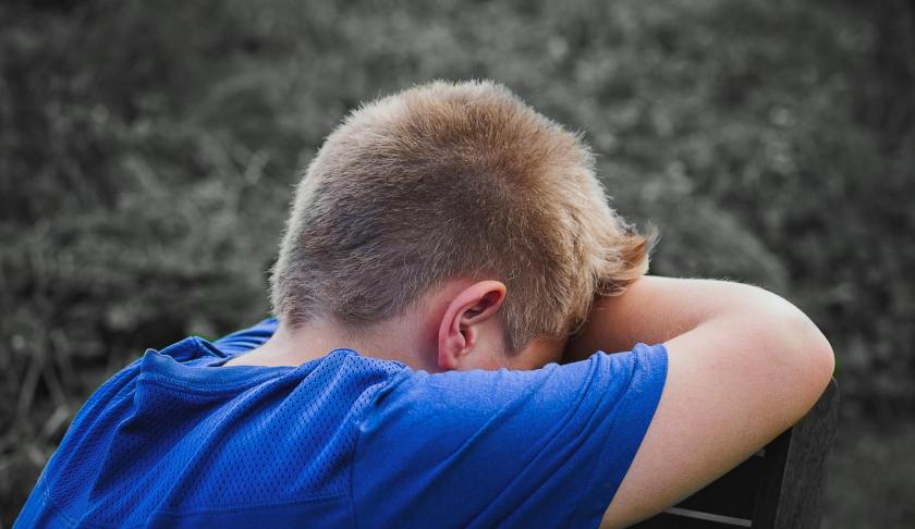 close up photo of sad child leaning on a wooden chair